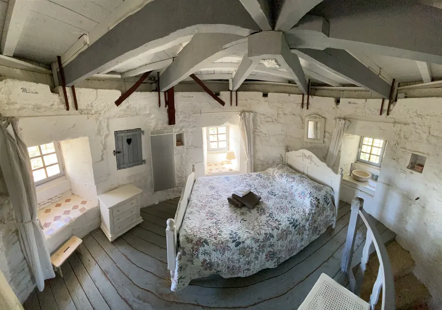 Chambre lumineuse sous la charpente du moulin, lit double et murs blanchis